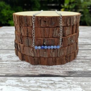 Handmade Blue Aventurine Necklace. Features a row of Blue Aventurine beads on a stainless steel wire. This is suspended from stainless steel chain. Necklaced shown draped over stack of wood slices.