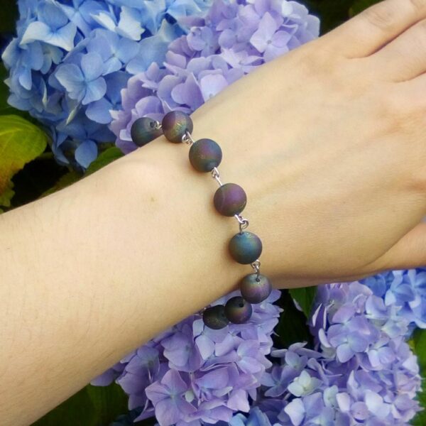 Handmade beaded bracelet worn on wrist. Bracelet features purple/blue toned Druzy beads.