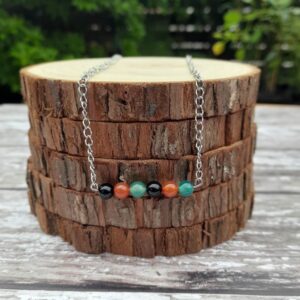 Handmade Mixed Agate Necklace. This necklace features a row of Mixed Agate beads on a stainless steel wire bar. This is suspended from a stainless steel curb chain. Necklace shown draped over stack of wood slices.