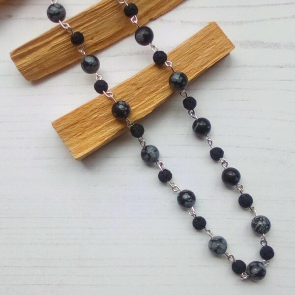Handmade Snowflake Obsidian and Lava Stone beaded necklace. Necklace draped over pieces of Palo Santo.