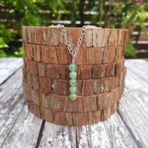 Handmade Green Aventurine Necklace. Necklace features a row of round Green Aventurine beads on a stainless steel wire suspended from stainless steel chain. Necklace shown draped over a stack of wood slices.