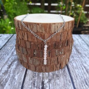 Handmade Rose Quartz Necklace. Necklace features a row of Rose Quartz beads on a stainless steel wire suspended from a stainless steel chain. Necklace shown draped over stack of wood slices.