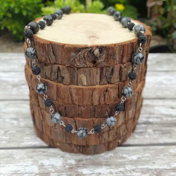 Handmade Snowflake Obsidian and Lava Stone beaded necklace. Necklace draped over stack of wood slices.